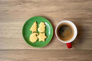 feliz natal com biscoitos caseiros e xícara de café no fundo da mesa de madeira. véspera de natal, festa, feriado e feliz ano novo conceito foto