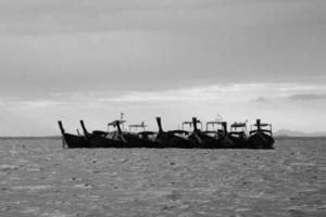 barcos de cauda longa flutuando no mar com onda e céu ao pôr do sol ou nascer do sol. beleza na natureza em tom preto e branco. transporte e fazer viagem no dia de férias. vista da paisagem de beleza. foto