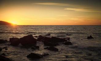 pedras costeiras e água do mar ao pôr do sol, Marrocos foto
