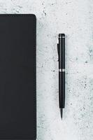 bloco de notas preto com uma caneta preta em um fundo cinza. foto