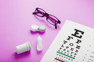 óculos de acessórios de oftalmologista, lentes e vitaminas com um alvo de teste para correção de visão em um fundo rosa. foto