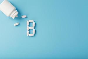 pílulas de vitamina b caíram de um frasco branco sobre um fundo azul. a letra na inscrição. foto
