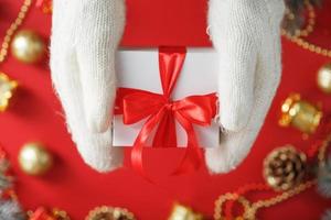 mãos em luvas de malha brancas segurando um presente em um fundo vermelho. foto