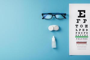 óculos com lentes de contato, gotas e gráfico de teste de olho de um optometrista em um fundo azul. foto