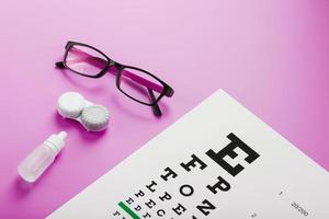 óculos de acessórios de oftalmologista, lentes e vitaminas com um alvo de teste para correção de visão em um fundo rosa. foto