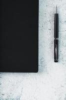 bloco de notas preto com uma caneta preta em um fundo cinza. foto