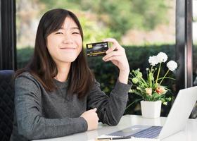 jovem mulher segurando cartão de crédito com computador portátil no convés foto