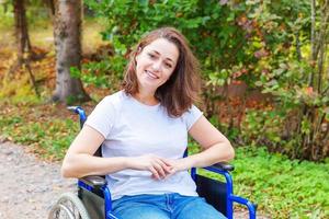 mulher jovem deficiente feliz em cadeira de rodas na estrada no parque hospitalar à espera de serviços ao paciente. menina paralisada na cadeira inválida para pessoas com deficiência ao ar livre na natureza. conceito de reabilitação. foto