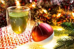 copo de vidro transparente de parede dupla com chá matcha japonês na mesa com decoração de natal. atmosfera de ano novo, guirlanda e enfeites, ramo de abeto, aconchegante, cobertor de malha, bola, guardanapo listrado foto