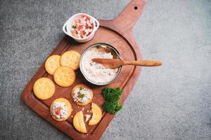 vista superior do saboroso atum espalhado com bolachas na bandeja de madeira e fundo de pedra preta com espaço de cópia, comida saudável e conceito de apetite foto