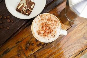 cappuccino quente em copo branco com fundo de madeira, o café é uma bebida popular em todo o mundo. foto