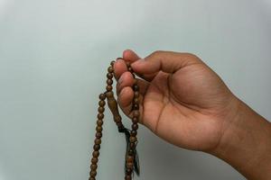 mão segurando contas de madeira tasbih isoladas. contas de oração islâmicas. conceito de oração muçulmana foto