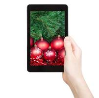 mão segura o tablet pc com enfeites de natal vermelhos foto