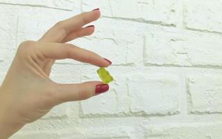 um ursinho amarelo gomoso nas mãos de uma garota com manicure vermelha. ursinho de pelúcia é segurado na mão contra o fundo de uma parede de tijolo branca feita de gesso. sobremesa doce doce para chá e café foto