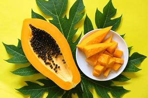 frutas de mamão em backgroud amarelo, fruta tropical fatia de mamão maduro fresco com sementes de mamão e folhas de papaia - vista superior foto