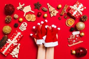 vista superior das mãos femininas segurando uma pilha de chapéus de Papai Noel em fundo vermelho. decorações de ano novo. conceito de férias de natal foto