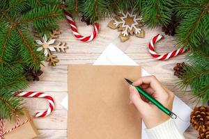 mão de menina escrevendo carta de natal em papel ofício com decorações em fundo de madeira