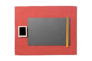 placa de ardósia preta retangular vazia com pauzinhos para sushi e molho de soja em fundo de guardanapo vermelho. vista superior com espaço de cópia para você projetar foto