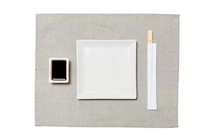 prato quadrado branco vazio com pauzinhos para sushi e molho de soja em fundo cinza guardanapo. vista superior com espaço de cópia para você projetar foto