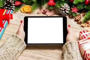 vista superior das mãos femininas segurando um tablet no fundo de madeira de natal feito de abeto e decorações festivas. conceito de férias de ano novo. brincar foto