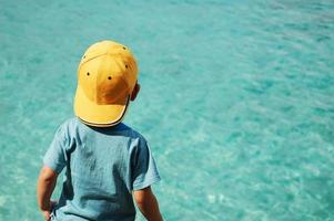 menino de boné amarelo na praia ou piscina foto