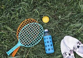 A planície de verão estava na grama verde com raquetes e bola, garrafa de vidro de água e sapatos brancos de verão foto