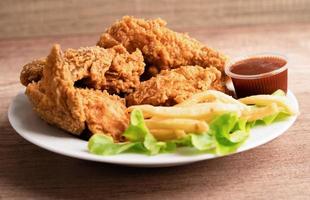 Frango frito e batata frita com folha de alecrim, junk food de alto teor calórico servido no prato branco foto