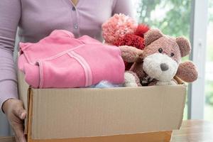 segurando caixa de doação de roupas com roupas usadas e boneca em casa para apoiar a ajuda aos pobres no mundo. foto