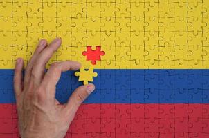 a bandeira da colômbia é retratada em um quebra-cabeça, que a mão do homem completa para dobrar foto