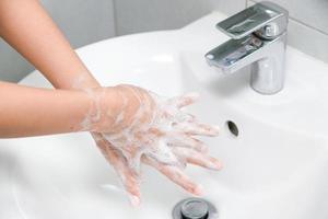 mulher usa sabão e lava as mãos sob a torneira de água. foto