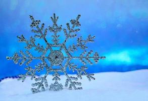 grande floco de neve brilhante na neve e céu azul por trás. fundo desfocado. cartão de feliz natal. bokeh de ano novo. espaço de cópia foto