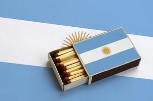 A bandeira argentina é mostrada em uma caixa de fósforos aberta, que está cheia de fósforos e fica em uma grande bandeira foto
