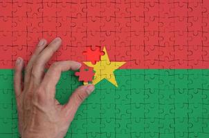 a bandeira de burkina faso é retratada em um quebra-cabeça, que a mão do homem completa para dobrar foto