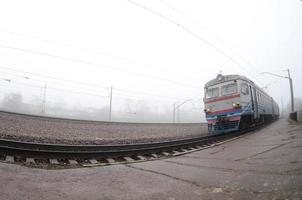 o trem suburbano ucraniano corre ao longo da ferrovia em uma manhã nublada. foto olho de peixe com distorção aumentada