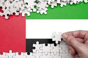 bandeira dos emirados árabes unidos é retratada em uma mesa na qual a mão humana dobra um quebra-cabeça de cor branca foto