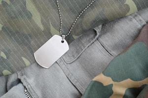 contas militares prateadas com placa de identificação em diferentes uniformes de fadiga de camuflagem foto
