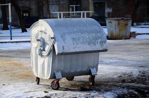 um recipiente de lixo prateado fica perto de edifícios residenciais no inverno foto