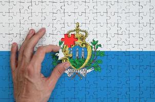 bandeira de san marino é retratada em um quebra-cabeça, que a mão do homem completa para dobrar foto