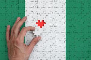 a bandeira da nigéria é retratada em um quebra-cabeça, que a mão do homem completa para dobrar foto