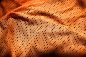 fundo de textura de tecido de roupas esportivas. vista superior da superfície têxtil de pano de nylon poliéster laranja. camisa de basquete colorida com espaço livre para texto foto