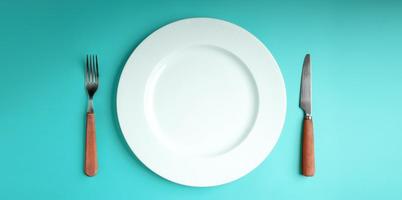 prato vazio branco com garfo e faca deitado no fundo da mesa azul. escassez de alimentos, questão da crise alimentar mundial. vista de mesa foto