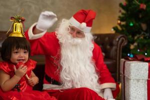 garotinha sentada junto com o papai noel no chão. celebre o feriado de natal e a festa de ação de graças. foto