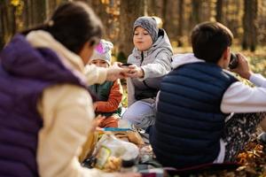 mãe com filhos em piquenique em família na floresta de outono. foto