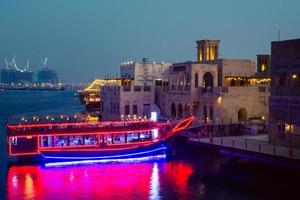 dubai, emirados árabes unidos, 2022 - restaurante de embarcações vintage iluminado - barco ancorado por belos edifícios antigos no antigo distrito de dubai creek no verão foto