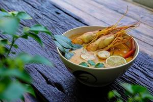 tom yum kung em um copo no chão de madeira, tom yum kung também é o prato nacional da tailândia. e é um alimento que é famoso em todo o mundo. foto