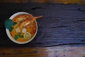 tom yum kung em um copo no chão de madeira, tom yum kung também é o prato nacional da tailândia. e é um alimento que é famoso em todo o mundo. foto