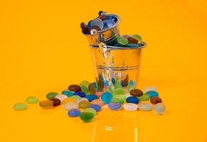 pedras coloridas em vidro em jarra em balde em fundo laranja foto