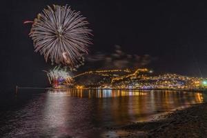 maravilhoso reflexo de fogos de artifício noturnos no mar e vista para o mar da cidade foto