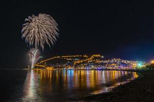 maravilhoso reflexo de fogos de artifício noturnos no mar e vista para o mar da cidade foto