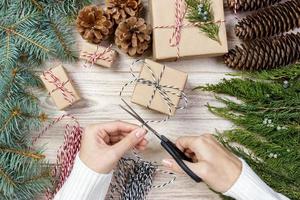 fundo de embrulho de presente de natal. mãos femininas embalagem presente de natal embrulhado em papel kraft vista superior. conceito de férias de inverno mulher plana leiga segurando a caixa de presente de natal foto